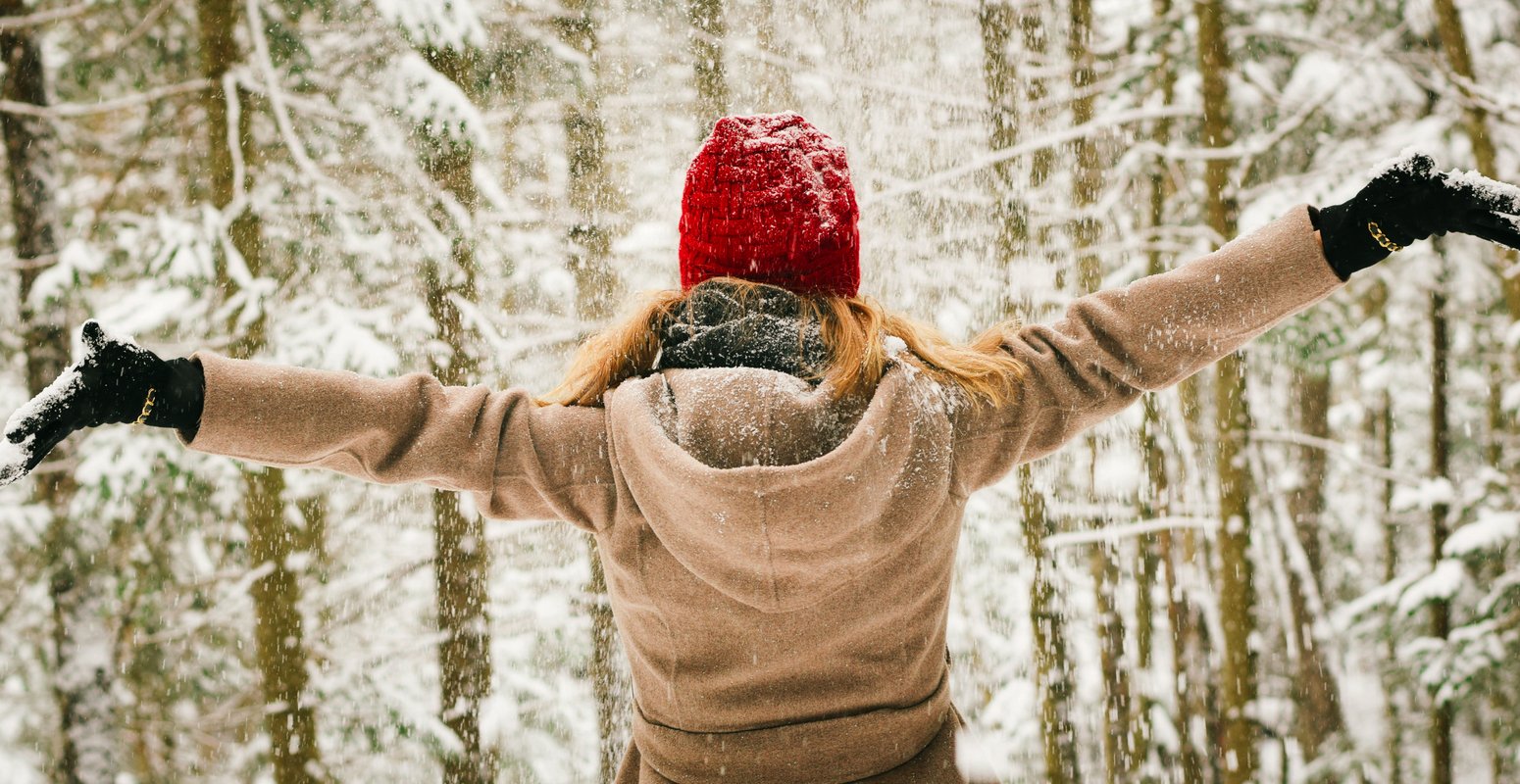 Frau hebt im verschneiten Wald ihre Arme 