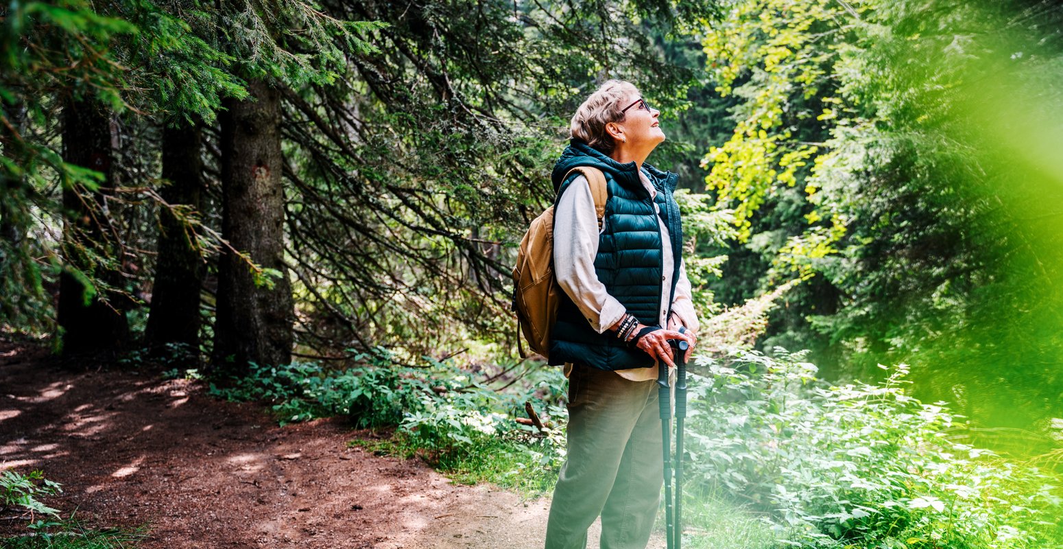 Frau steht mit Wanderstock im Wald