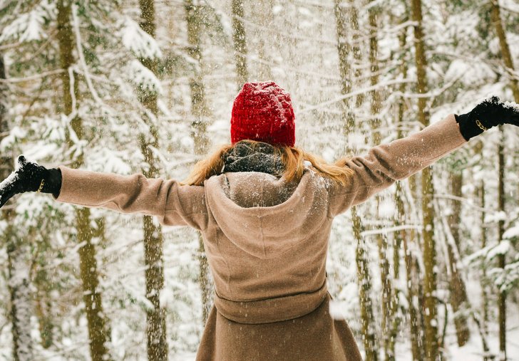 Frau hebt im verschneiten Wald die Arme